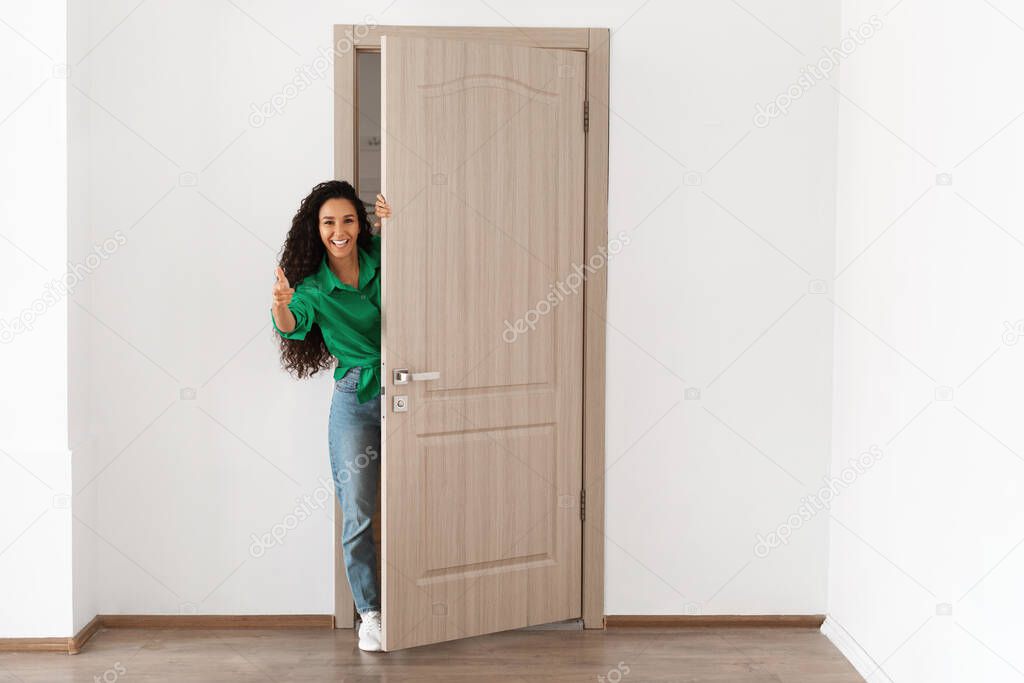 Cheerful lady looking out of door pointing finger at camera