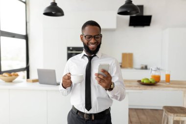 Siyah adam akıllı telefonuyla kahve içerken mesaj atıyor.