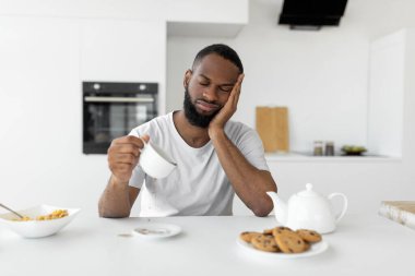 Black man yawning, pouring coffee away from cup clipart