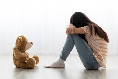 Sad long-haired little girl sitting with toy, crying