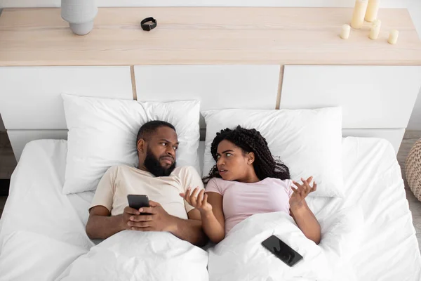 Angry sad millennial black woman gesturing and look at husband for addiction to phone, online game — Stock fotografie