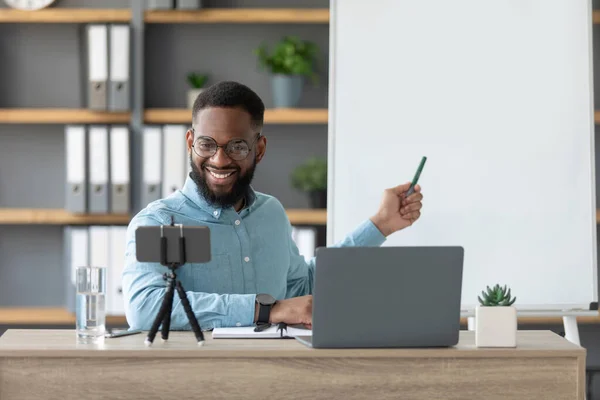Friendly χαρούμενα χιλιετή αφροαμερικανός δάσκαλος άνθρωπος δείχνουν στους αγγλικούς κανόνες, κοιτάζει PC και smartphone κάμερα — Φωτογραφία Αρχείου