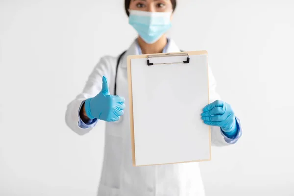 Cropped young cute indian lady doctor in uniform, gloves, protective mask shows tablet with blank space and thumb up —  Fotos de Stock