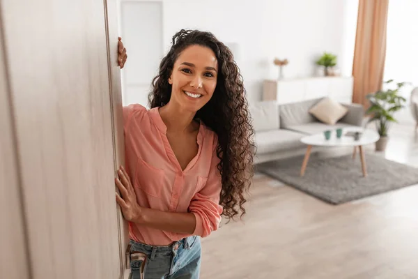 Cheerful young curly lady inviting people to enter home — Foto Stock