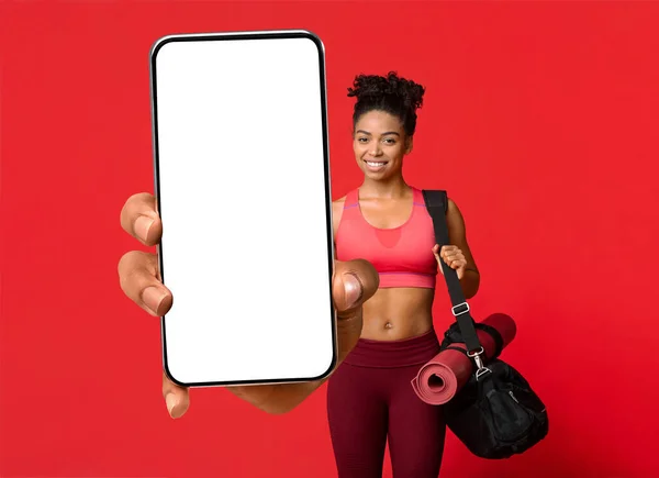 Happy black sportswoman showing smartphone with empty screen, mockup for mobile fitness app or website design — Photo