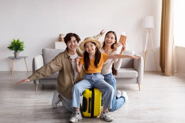 Happy teen girl in hat hold plane sitting on suitcase, young asian lady and man rejoice, have fun and show passport — Zdjęcie stockowe