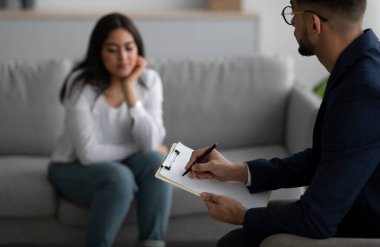Psychological therapy. Male psychologist noting problems of young arab woman at psychotherapy session, selective focus
