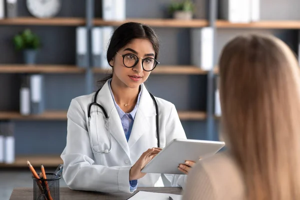 Friendly attentive millennial cute indian female therapist in uniform and glasses, consults patient in clinic — Stockfoto