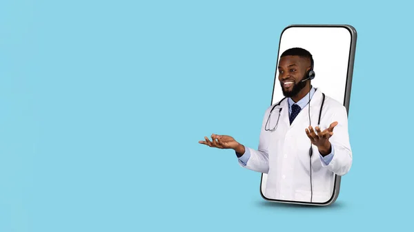 Τηλεϊατρική έννοια. Μαύρος γιατρός σε ακουστικά κρυφοκοιτάζοντας από μεγάλη οθόνη Smartphone — Φωτογραφία Αρχείου