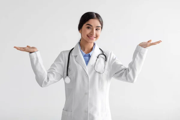 Усміхнений молода індійська жінка-лікар показує обидві руки відкриті долоні, представляючи порівняння та рекламний баланс — стокове фото