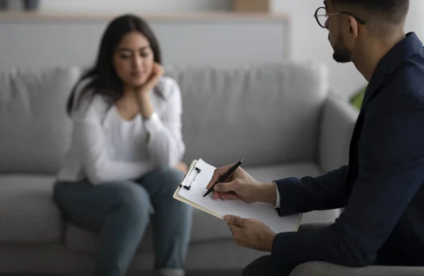 Psychological therapy. Male psychologist noting problems of young arab woman at psychotherapy session, selective focus — Photo