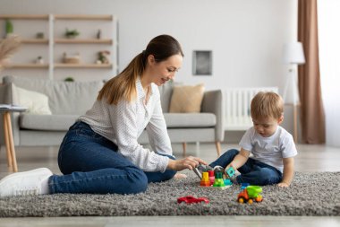 Young mother and her son playing with wooden stacking and sorting toy at home, sitting on floor carpet