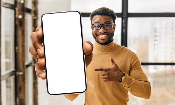 Διαφήμιση εφαρμογών για κινητά. Μαύρος άνδρας που δείχνει και δείχνει τη μεγάλη λευκή άδεια οθόνη smartphone, mockup, closeup — Φωτογραφία Αρχείου