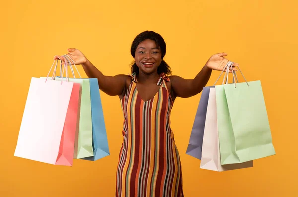 Seasonal sales and shopping. Charming young black woman showing bright shopper bags with purchases at camera — Stockfoto