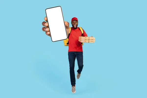 Order Pizza Online. Cheerful Black Delivery Guy Jumping And Showing Blank Smartphone