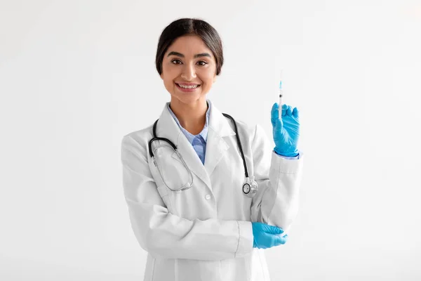 Sonriente joven hindú trabajadora médica en uniforme, guantes protectores, muestra jeringa con vacuna —  Fotos de Stock