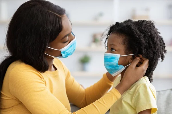 Caring Black Mother Putting On Face Mask On Her Little Daughter —  Fotos de Stock