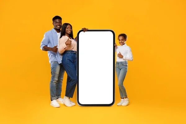 Family leaning on white empty smartphone screen showing thumbs up — Stockfoto