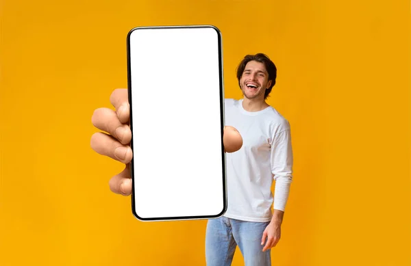 Διαφήμιση εφαρμογών. Ενθουσιασμένος άνθρωπος κρατώντας smartphone με λευκή κενή οθόνη στο χέρι κοντά στην κάμερα, mockup — Φωτογραφία Αρχείου
