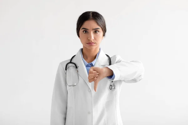 Triste infeliz enojado joven atractivo indio mujer médico trabajador en uniforme con estetoscopio mostrar pulgar hacia abajo —  Fotos de Stock