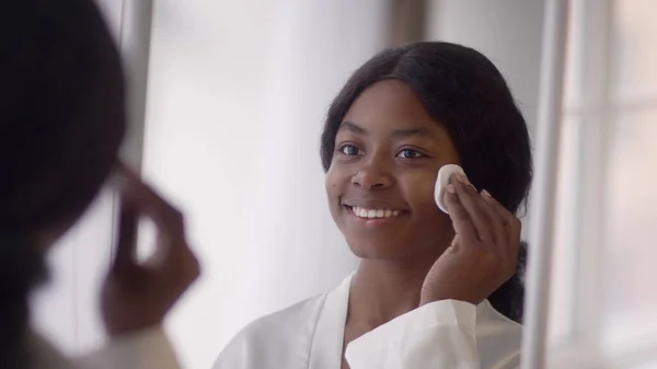 Cheerful Black Woman Removing Makeup With Cotton Pad In Bathroom — Stok fotoğraf