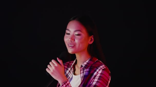 Талановита молода азіатська леді співає мікрофон стоячи над темним тлом — стокове відео