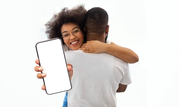 Bonita dama negra abrazando a su novio y mostrando teléfono inteligente, maqueta — Foto de Stock