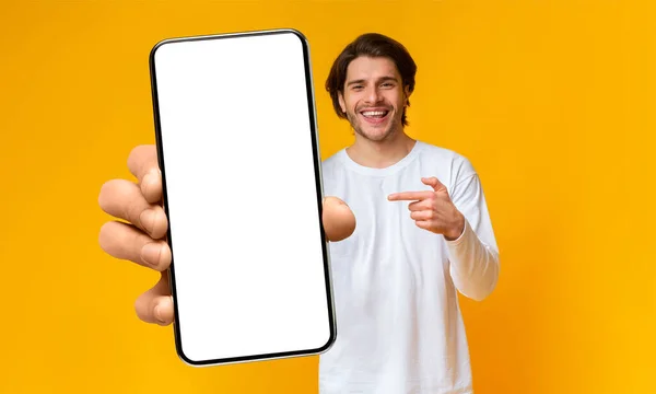 Handsome positive man showing cellphone with white blank screen and pointing on it, mockup, closeup, selective focus — Fotografia de Stock