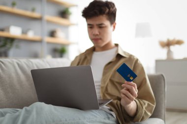 Odaklanmış Asyalı adam evde kredi kartı kullanıyor.