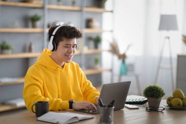 Smiling asian man in headset using laptop at home