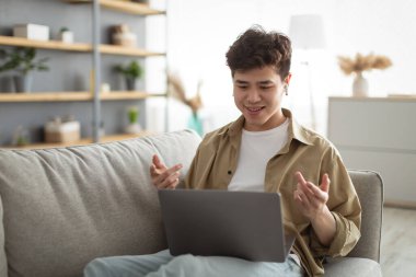 Asian man having videochat using laptop and talking at webcam