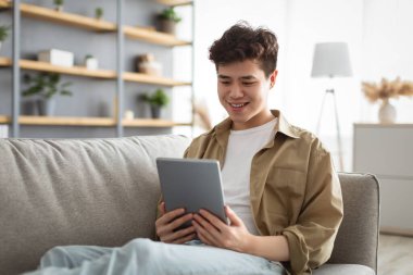 Evde dijital tablet kullanan gülümseyen Asyalı adam.