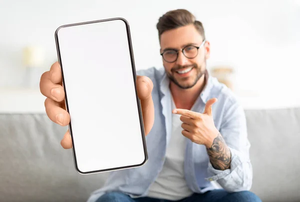 Hombre joven guapo señalando en el teléfono inteligente con gran pantalla en blanco en casa — Foto de Stock