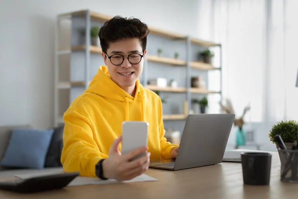 Hombre asiático en gafas sentado en el escritorio usando el teléfono celular — Foto de Stock