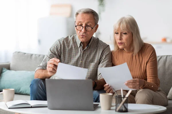 Senior Spouses Reading Papers And Bills Sitting Near Laptop Indoors