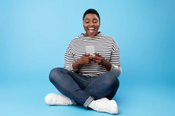Αφρικανική αμερικανική γυναίκα χρησιμοποιώντας τηλέφωνο κάθεται κείμενο πάνω από το μπλε φόντο — Φωτογραφία Αρχείου