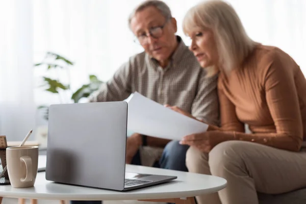 Senior Couple Reading Papers Using Laptop Sitting On Couch Indoors — Foto Stock