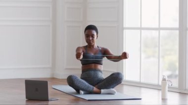 Sporty black woman training with resistance rubber band in front of laptop