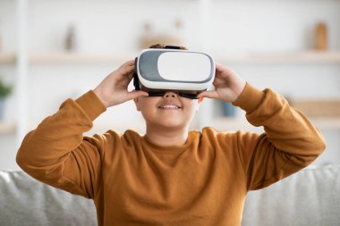 Happy overweight boy with VR glasses, home interior