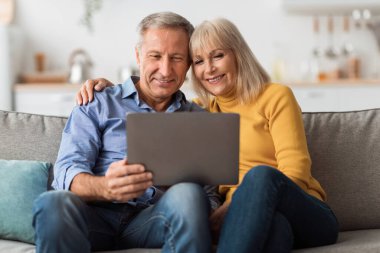 Senior Husband And Wife Using Laptop Computer Embracing At Home
