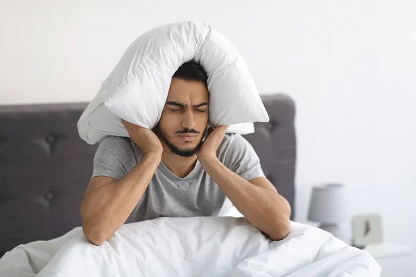ベッドの上に座り、枕で耳を覆うアラブ人の男 — ストック写真