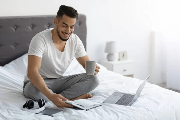 Remote Work. Arab Freelancer Man Working With Laptop And Notepad In Bed — Stock Photo, Image