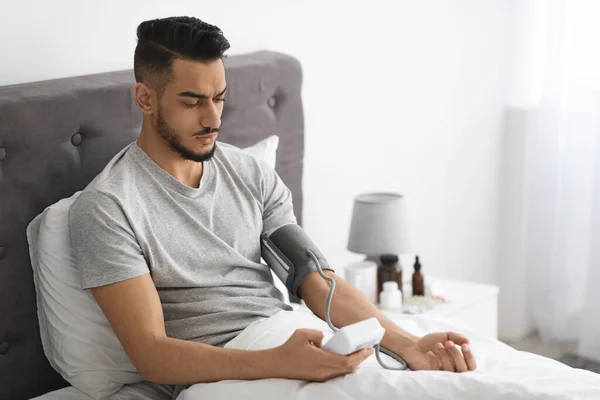 Arab Man Using Upper Arm Blood Pressure Monitor While Sitting In Bed — Stock Fotó