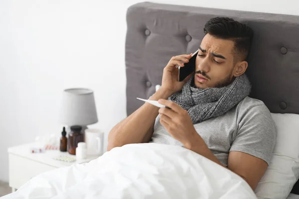 Online Consultation. Sick Arab Man Holding Thermometer And Calling Doctor On Phone — Stock fotografie