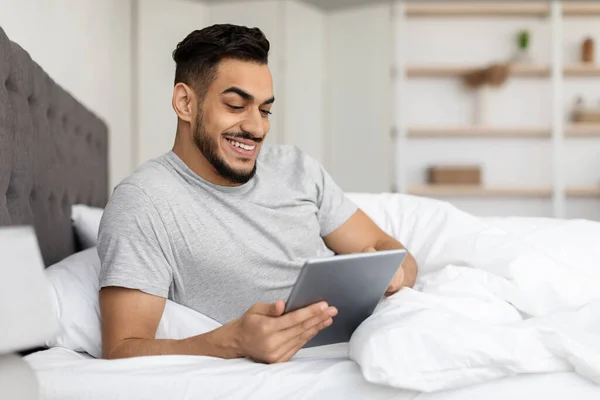 Handsome Young Middle Eastern Guy Relaxing In Bed With Digital Tablet — Zdjęcie stockowe