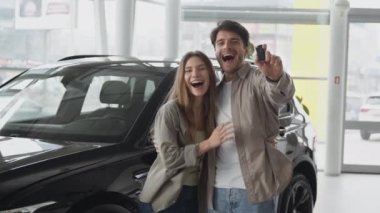 Excited young couple in love celebrating successful car purchase, dancing and having fun at auto dealership, zoom in
