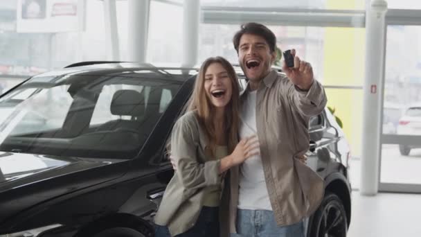 Excited young couple in love celebrating successful car purchase, dancing and having fun at auto dealership, zoom in — Vídeos de Stock