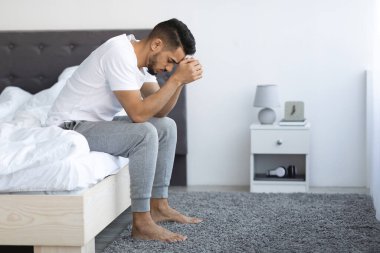 Life Problems. Upset Young Arab Man Sitting On Bed At Home
