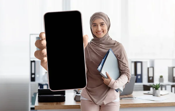Smiling arab businesswoman showing smartphone with big blank screen, demonstrating device with black touchscreen — Foto Stock
