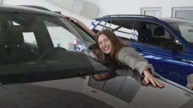 Happy owner. Young excited woman hugging new car, enjoying long awaited vehicle purchase at dealership salon, zoom in